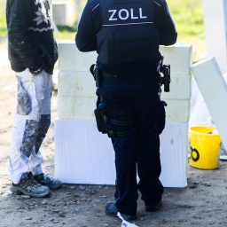 Ein Zollbeamter (r.) steht mit einem Bauarbeiter bei einer Kontrolle von Schwarzarbeit in einem Neubaugebiet in der Region Hannover.